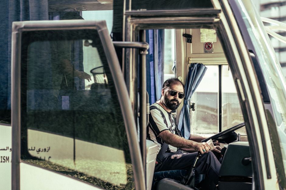Een buschauffeur van EBS die een bus bestuurt in de stad, met passagiers aan boord.
